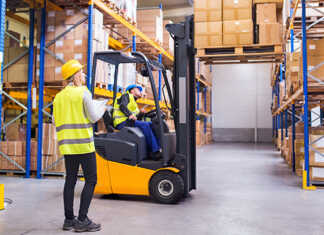 A worker operating a forklift while a co-worker looks on.